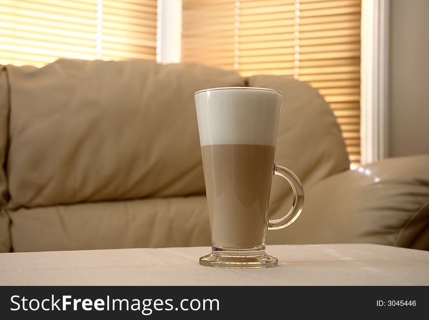 Cafe Latte in a tall glass and creamy sofa on background, soft focus