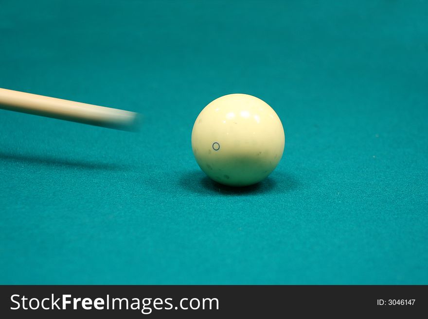 Pool stick striking cue ball on a green table