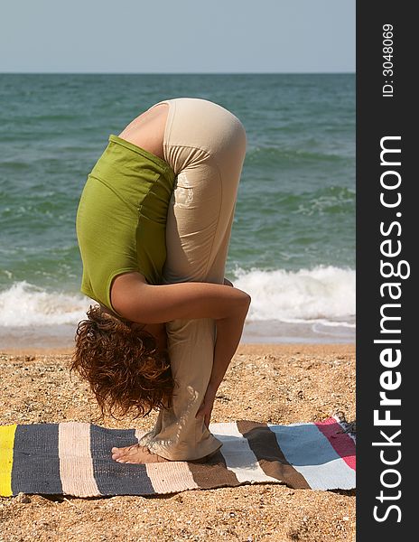 Girl doing Uttanasana yoga pose at sea coast