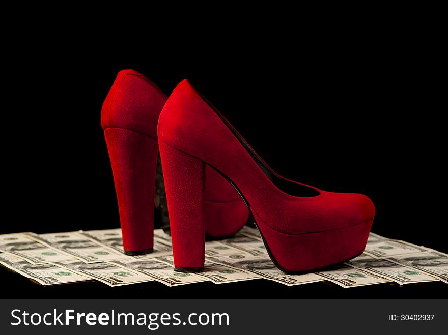 Pair of red female shoes and dollars on black background. Studio shot. Pair of red female shoes and dollars on black background. Studio shot.