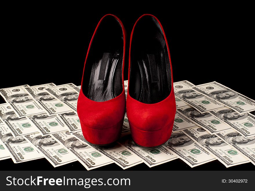 Pair of red female shoes and dollars on black background. Studio shot. Pair of red female shoes and dollars on black background. Studio shot.