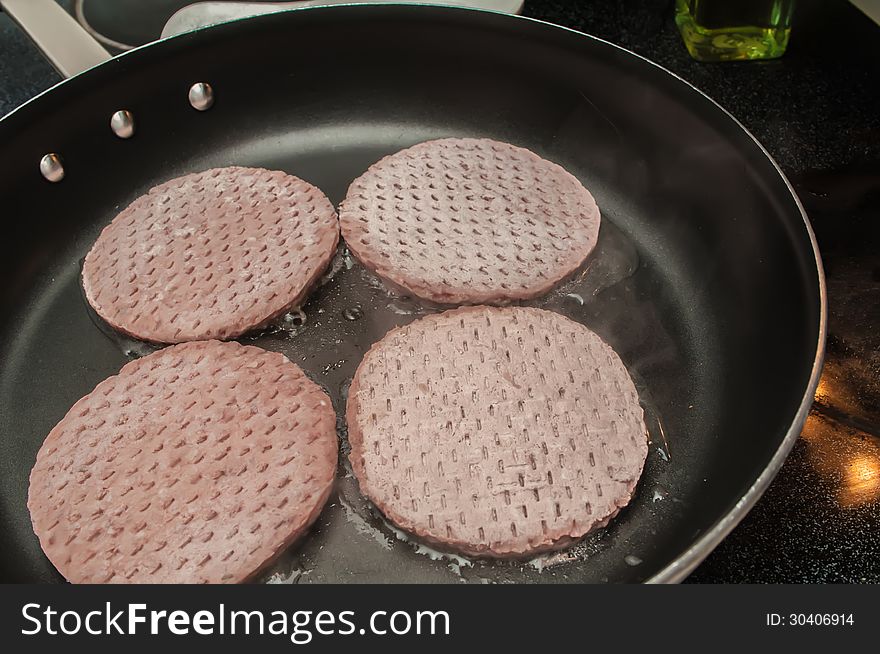 Four hamburgers in a hot frying pan. Four hamburgers in a hot frying pan.