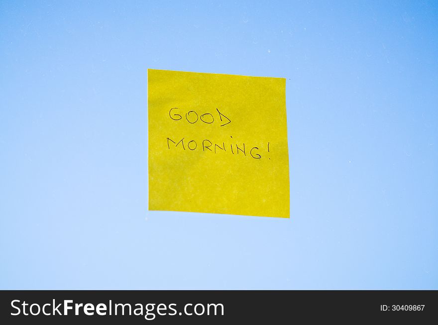 Good Morning text handwritten on a sticky note against blue background