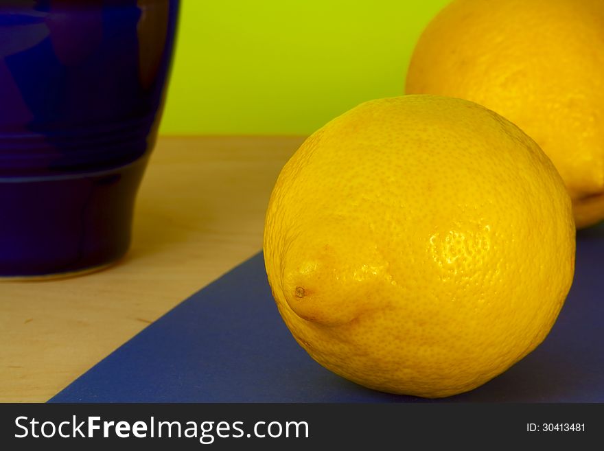 Two ripe lemons and blue pitcher on a colored background. Two ripe lemons and blue pitcher on a colored background