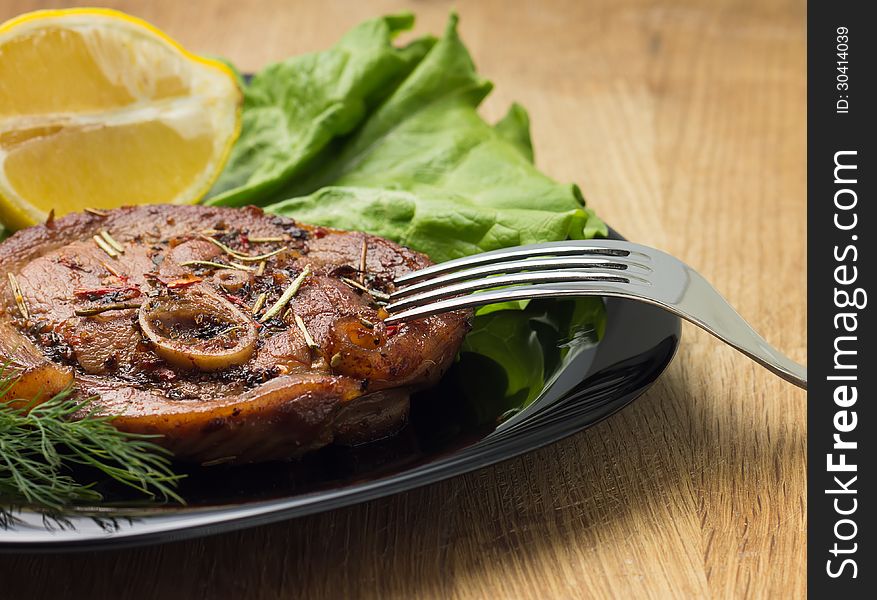 Grilled steak with salad and lemon at black plate with fork on wood background. Grilled steak with salad and lemon at black plate with fork on wood background