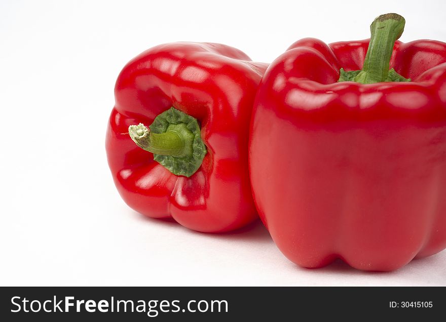 Bright Red Vegetable Peppers Sit in a Pair on a WHite Background. Bright Red Vegetable Peppers Sit in a Pair on a WHite Background