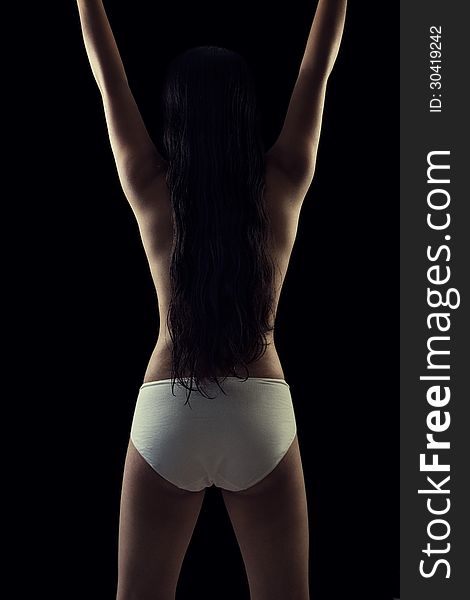 Back view of a indian modern nude girl raising up her arms against black. Back view of a indian modern nude girl raising up her arms against black