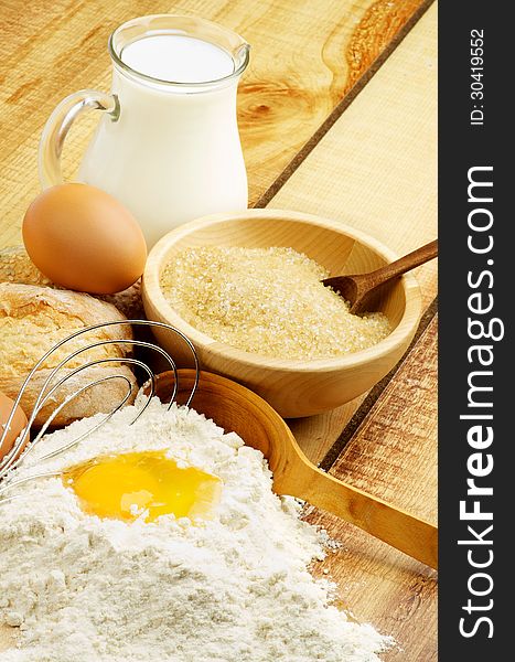Preparing Dough. Ingredients with Jar of Milk, Flour, Egg, Sugar and Wooden Spoon with Egg Whisk closeup on Wooden background
