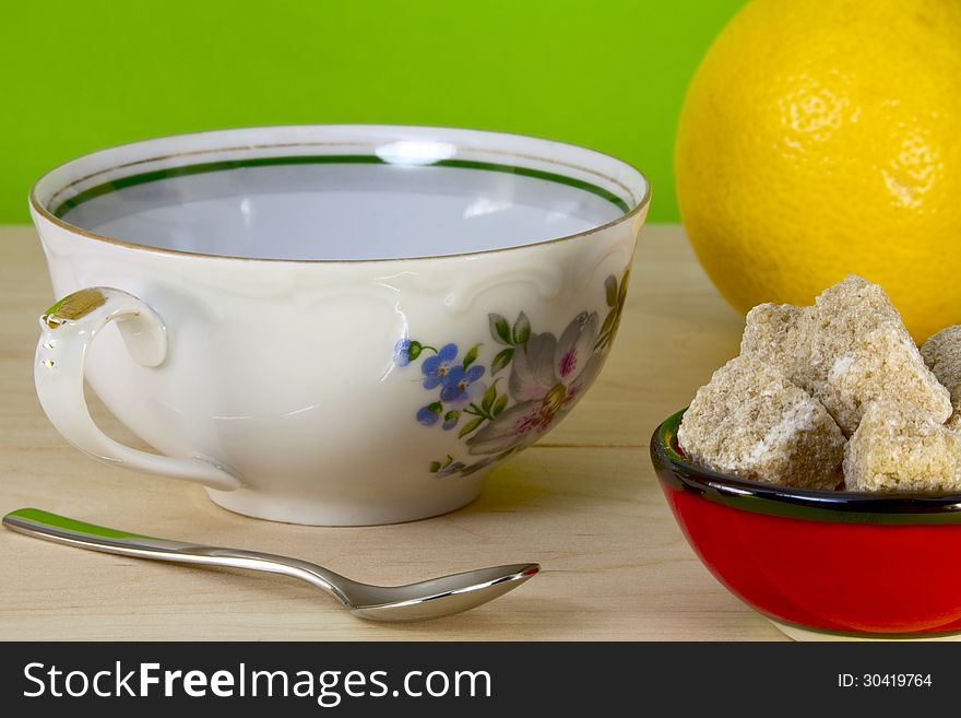 Tea cup, spoon, lemon and brown sugar on a green background. Tea cup, spoon, lemon and brown sugar on a green background