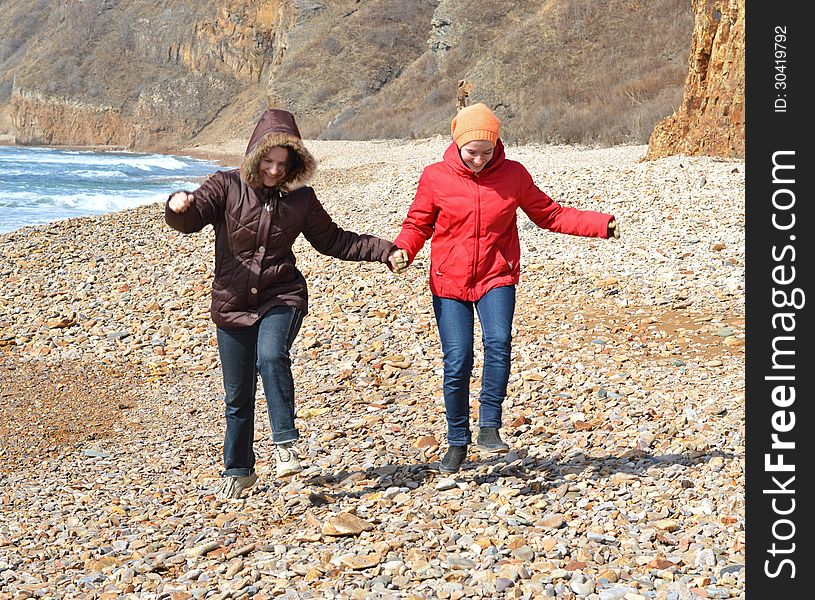 Two girls in red and purple coats jumping on the seashore. Two girls in red and purple coats jumping on the seashore