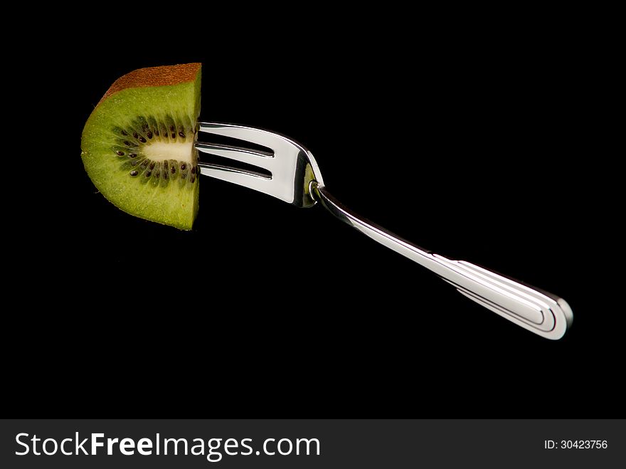 A piece of kiwi fixed on desert fork. Black background. Studio shot.