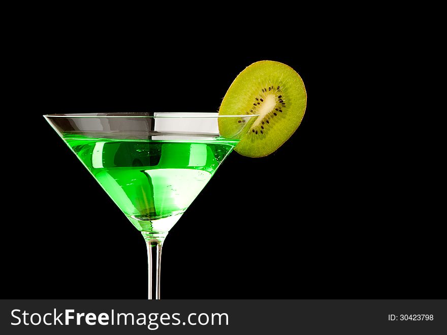 Glass filed with green beverage and a pieces of kiwi. Black background. Studio shot.