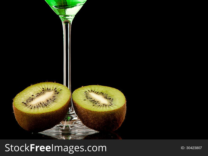 Glass filed with green beverage and a pieces of kiwi. Black background. Studio shot.