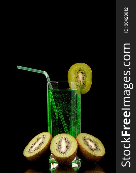 Glass filed with green beverage and a pieces of kiwi. Black background. Studio shot.