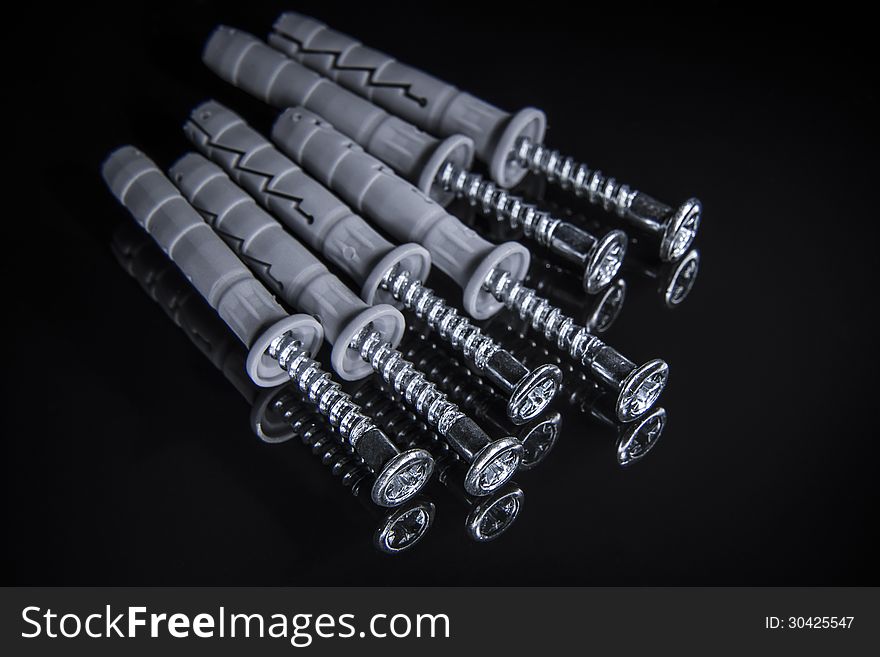 Close up of screws with plastic drywall plugs on black reflecting surface background. Close up of screws with plastic drywall plugs on black reflecting surface background.