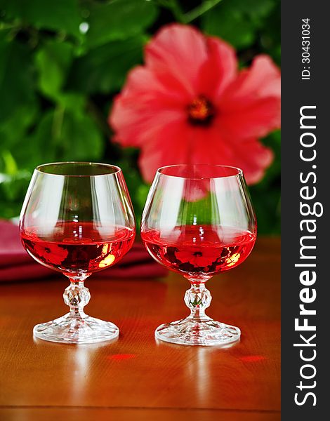 On the table glasses of red wine , the background - a flowering plant. On the table glasses of red wine , the background - a flowering plant