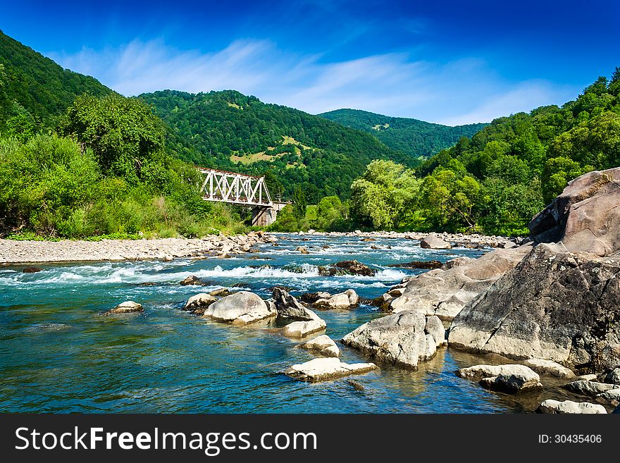 Shore of a mountain river with stones and iron bridge