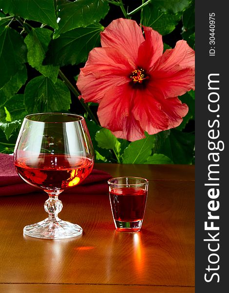 A glass with red wine and a small glass with liquor, the background - a flowering plant. A glass with red wine and a small glass with liquor, the background - a flowering plant