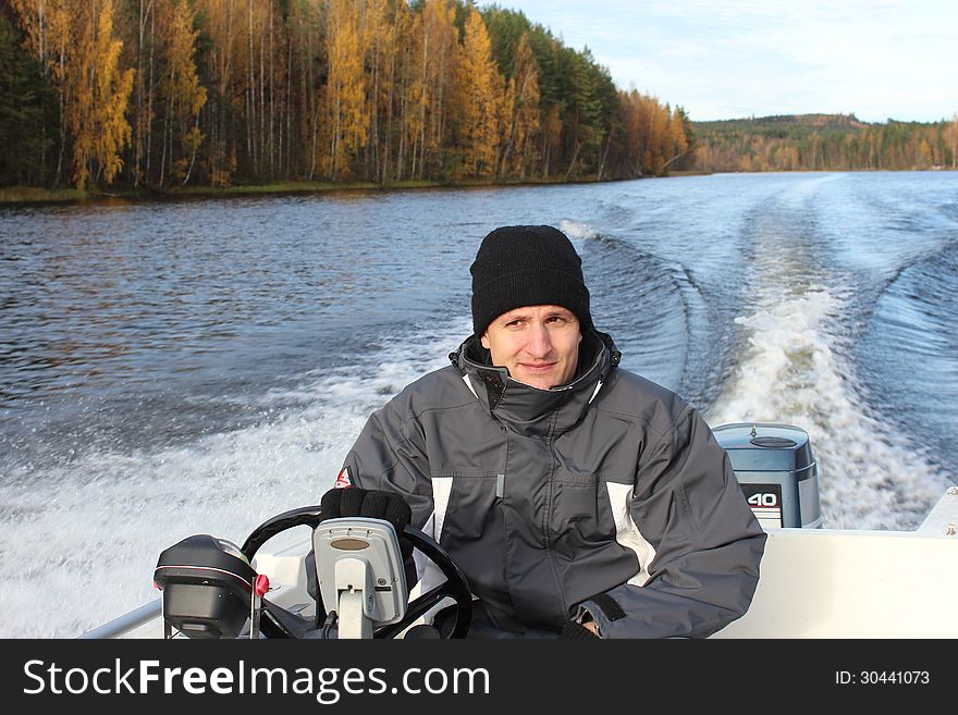 A man driving a boat on a calm autumnal lake. A man driving a boat on a calm autumnal lake
