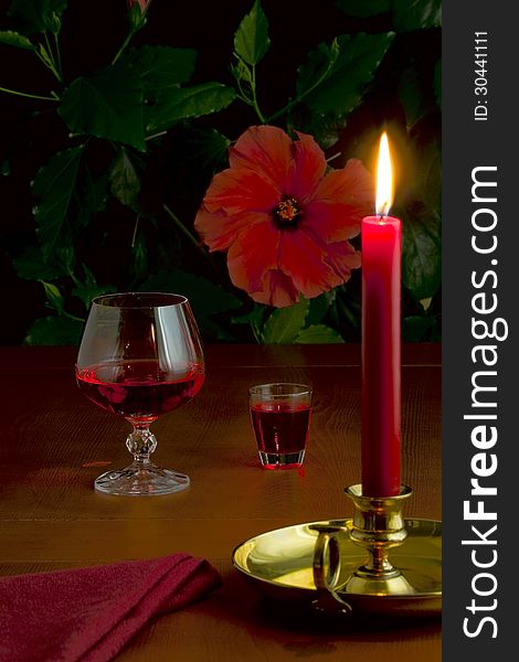 On the table a glass with red wine, a small glass with liquor and a burning candle in a candlestick. On the table a glass with red wine, a small glass with liquor and a burning candle in a candlestick