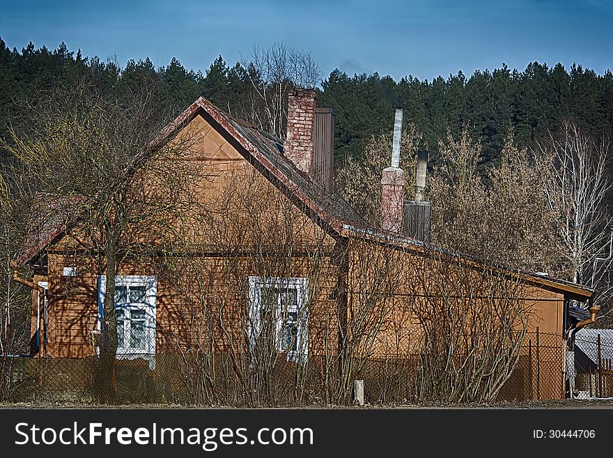 Rural landscape- old village house with springtime garden. Dense forest and clear blue sky background. Rural landscape- old village house with springtime garden. Dense forest and clear blue sky background.