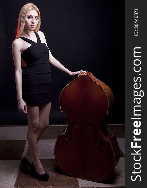 Blonde model next to a broken contrabass on a black background studio shot