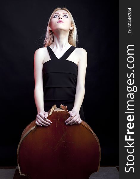 Elegant girl behind a broken contrabass on black background