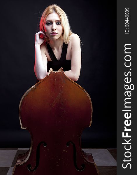 Elegant girl behind a broken contrabass on black background studio shot