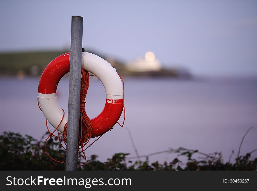 A red and white life ring hanging on a post, overlooking the ocean.