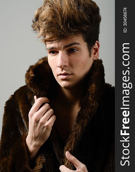 Attractive young man wearing fur coat with modern hairstyle