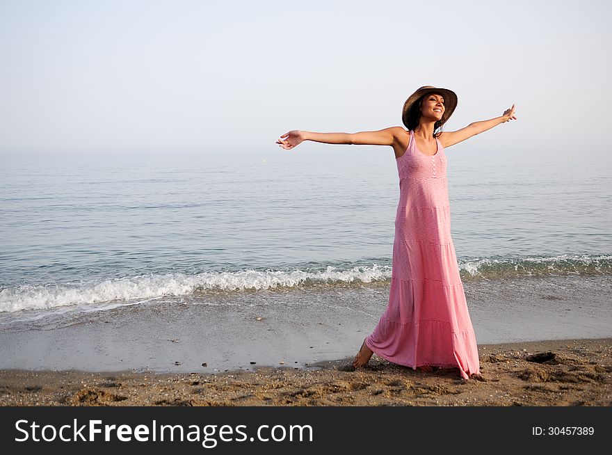 Portrait of a beautiful woman with long pink dress and sun hat on a tropical beach. Portrait of a beautiful woman with long pink dress and sun hat on a tropical beach