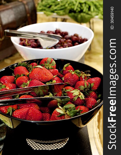 Black bowl of bright red strawberries with green attached. Black bowl of bright red strawberries with green attached.