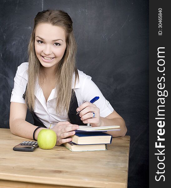 Portrait of happy cute young student near blackboard with copy book calculator pen, copy space