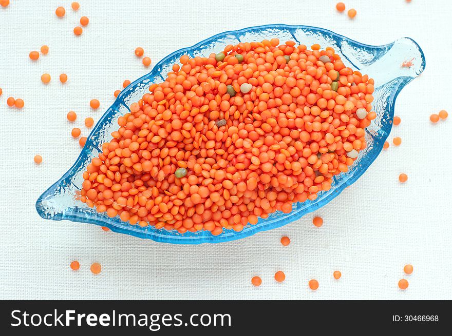 Upper view on raw red lentils in a leaf-shaped glass plate. Upper view on raw red lentils in a leaf-shaped glass plate