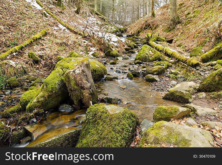 Stream running downhill over moss covered stones in winter. Stream running downhill over moss covered stones in winter