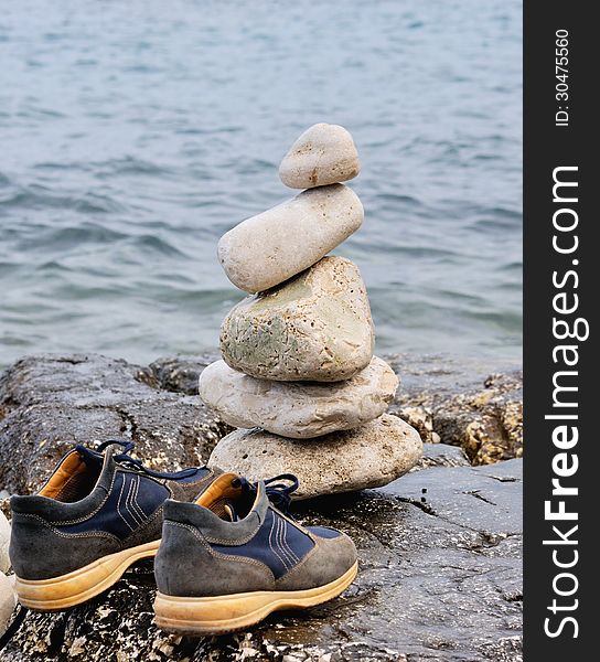 Stones in balance on the rocks of the sea with a pair of shoes