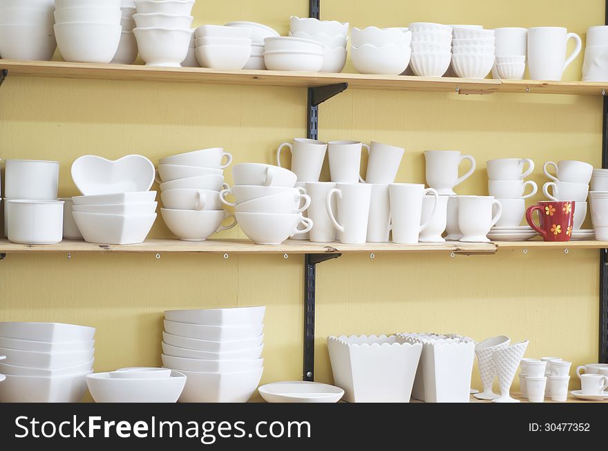 Three shelves of unfinished pottery that show one piece painted and glazed that stands out. Three shelves of unfinished pottery that show one piece painted and glazed that stands out.