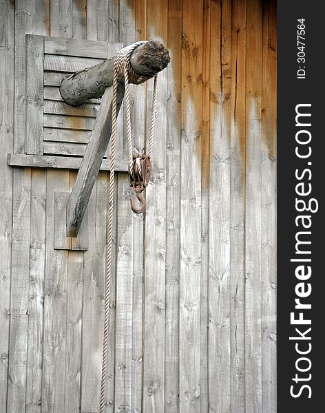 Horizontal pole through wooden wall with long rope rolled around it and iron hook attached to rope. Horizontal pole through wooden wall with long rope rolled around it and iron hook attached to rope