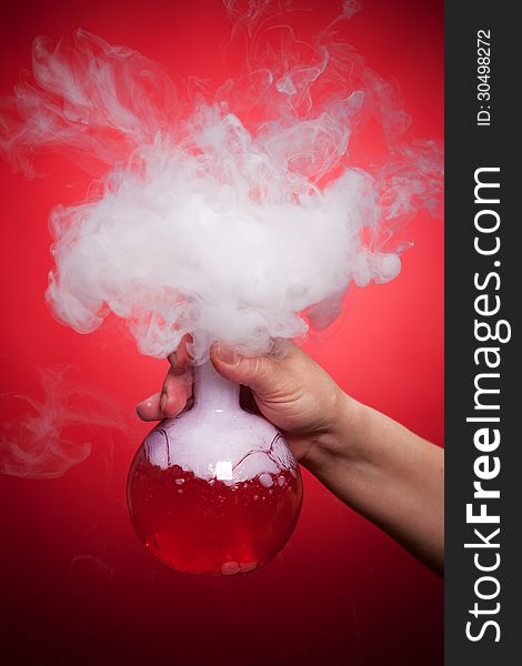 Steaming flask with red liquid in the hand on a red background