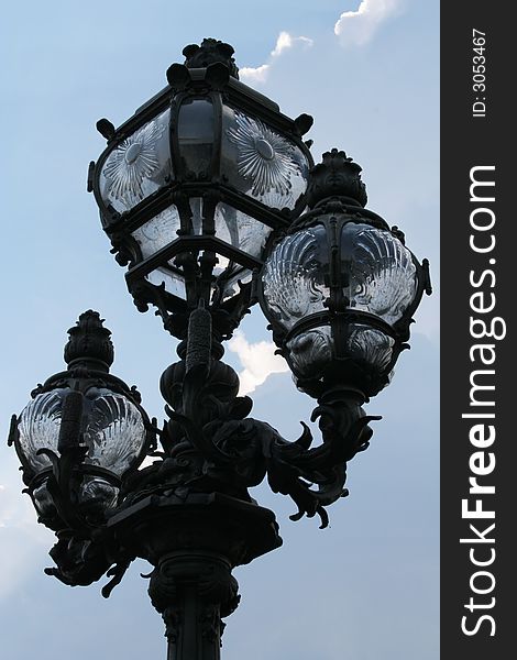 Lamp post in Paris made of forged iron and glass with a cloudy blue sky behind. It's on the Alexandre III bridge. Lamp post in Paris made of forged iron and glass with a cloudy blue sky behind. It's on the Alexandre III bridge.