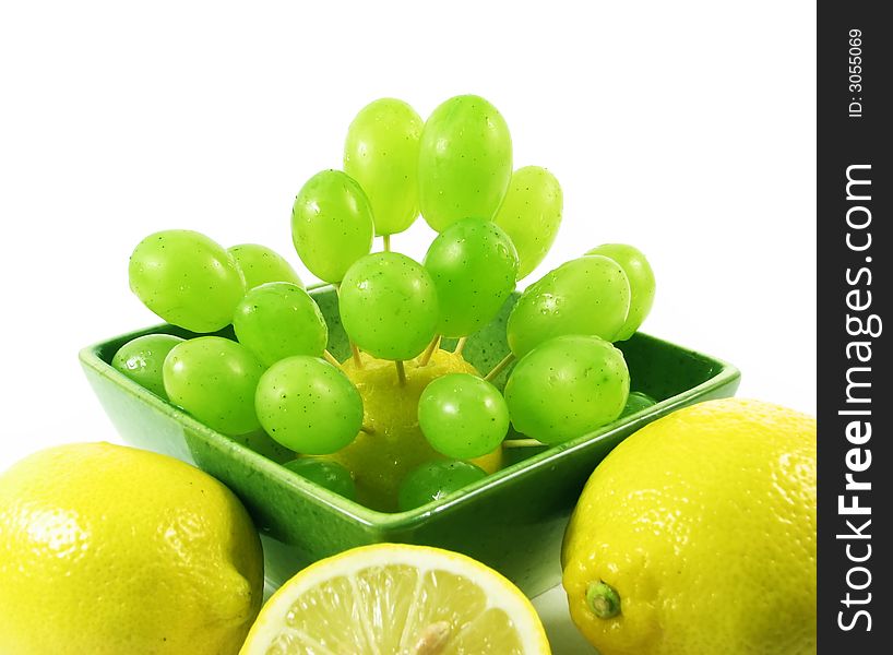 Grapes fruit and lemons in green bowl on white background