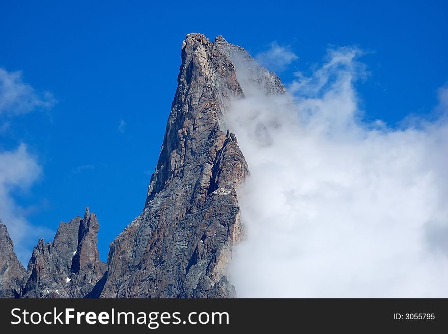 Aiguille Noire (Mont Blanc, Italy) rocky peak, while a growing cloud try to climb it.