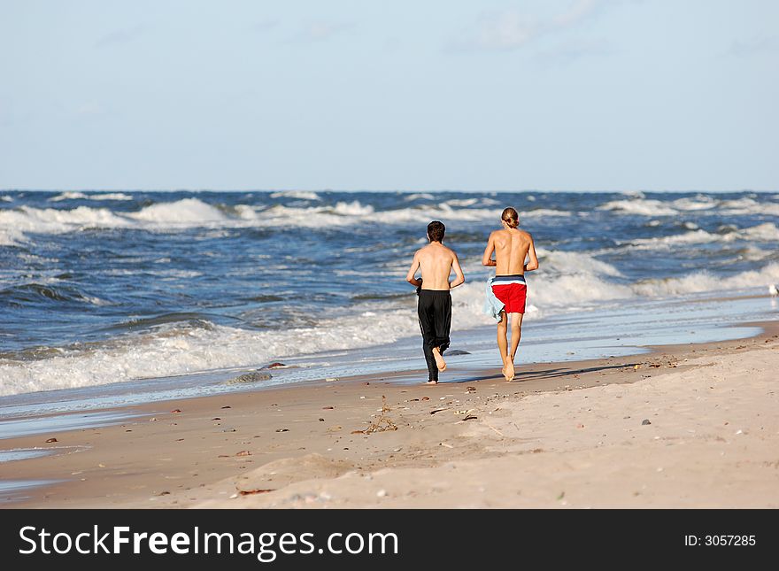 Two boys running on the beach with waved sea