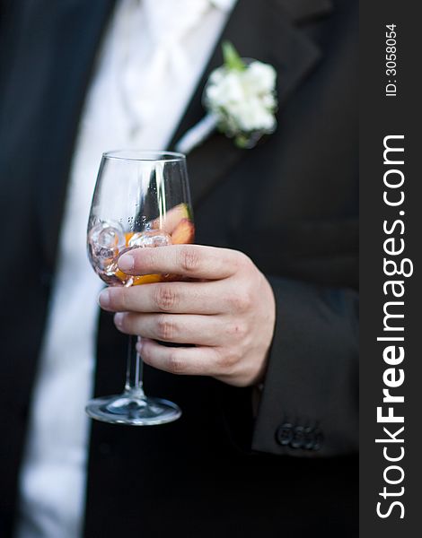 Bridegroom holding a glass of wine-cooler with icecubes. Close-Up. Shallow DOF!