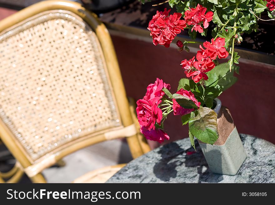 A chair with red flowers. It could be a tipical european bar, a restaurant or just a modern house corner. A representation of a summer relax moment.