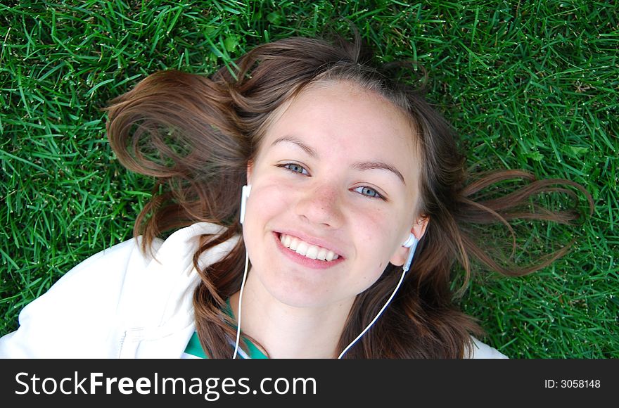 Young girl laying on the green grass and listening music