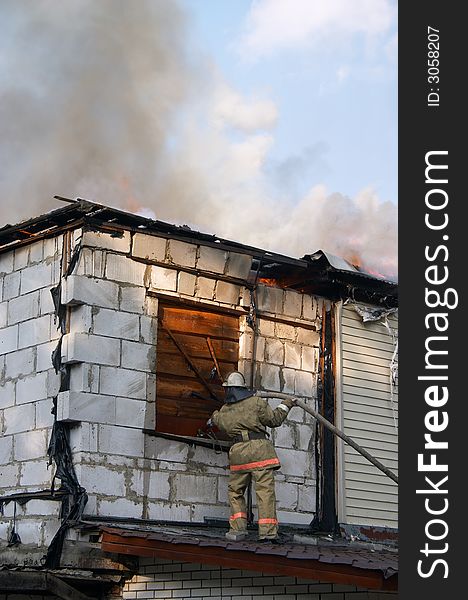Firefighter extinguishing a fire in flaming house. Firefighter extinguishing a fire in flaming house