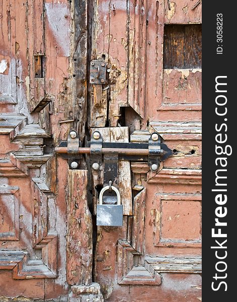 An old wood door with a rusty door latch and a padlock. An old wood door with a rusty door latch and a padlock