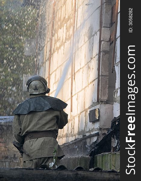 Fireman with fire hose spraying water on a flaming house