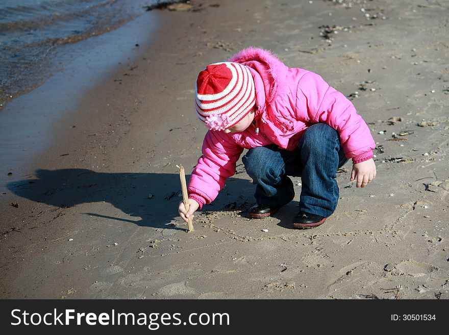 Little girl in a pink jacket draws in the sand. Little girl in a pink jacket draws in the sand